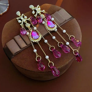 Detail of pink crystal tassel earrings with gold bow and pearls on a gift box