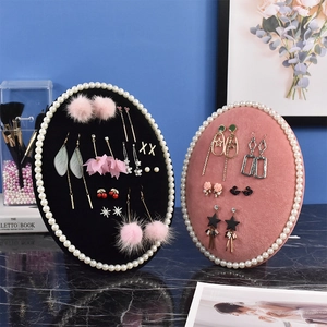 Pink and black velvet jewelry display stands with pearl edges on marble surface