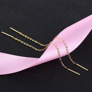 Close-up of minimalist gold threader earrings draped over a pink silk ribbon