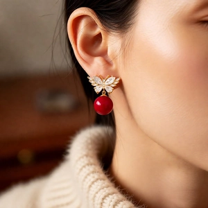 Close-up of golden butterfly earrings with red bead pendant and zircons on model
