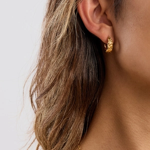Gros plan d'une boucle d'oreille créole dorée en acier titane portée par un mannequin pro