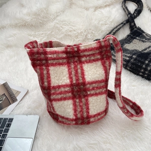 Detail view of a soft red and beige plaid plush bucket bag on a white textured carpet