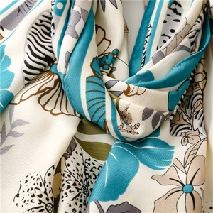 Detailed close-up showing the twill texture and teal tropical floral print on a silk scarf