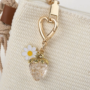 Detail of golden heart clasp with daisy charm and glittery strawberry on woven bag