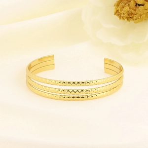 Detail of gold stacked bangle with diamond-pattern texture on satin background