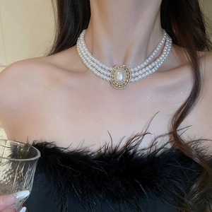 Detailed view of triple-layer pearl necklace with gold-framed pendant on model