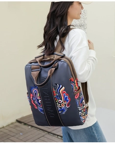 Side view of model wearing a dark grey backpack with colorful ethnic dragon embroidery