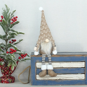 Gnomo di Natale con cappello in maglia marrone e lunghe gambe a strisce grigie su legno