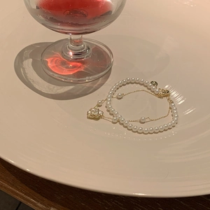 Détail d'un bracelet de perles à double rangée avec chaîne dorée et breloque camélia blanc
