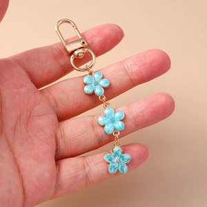 Close-up of gold metal keychain featuring three light blue enamel flower pendants