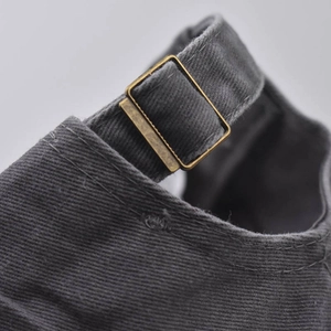Detail of adjustable vintage brass buckle on dark grey cotton twill baseball cap