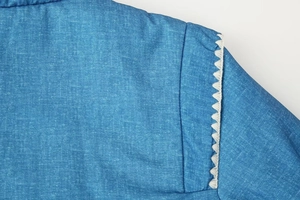 Makro-Detail des blauen Denim-Baumwollmantels mit weißem Häkelspitzen-Besatz an der Schulter