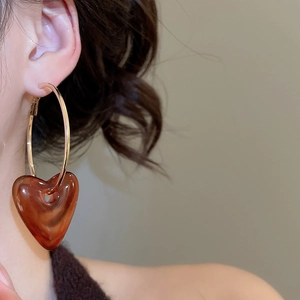 Close-up of amber resin heart pendant hanging from golden metal hoop earrings on model