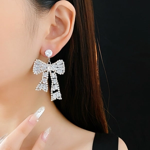 Close-up of sparkling rhinestone bow earrings worn by a model in silver finish