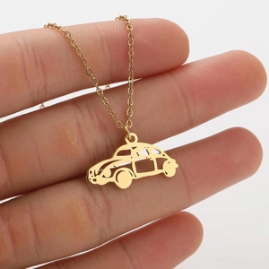 Detailed macro view of a gold-plated stainless steel car pendant necklace held by hand