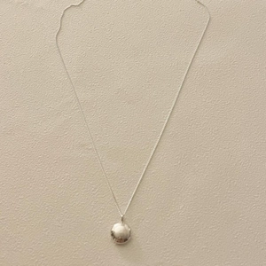 Close-up of minimalist 925 sterling silver key necklace with round pendant on beige surface