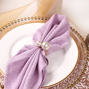 U-shaped golden napkin ring with white pearls on a purple linen napkin and gold placemat