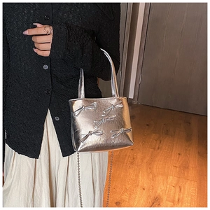 Close-up of silver pleated faux leather handbag featuring metal bow details and chain strap
