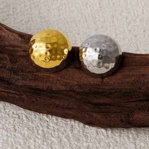 Close-up of gold and silver hammered dome earrings on a premium wooden display