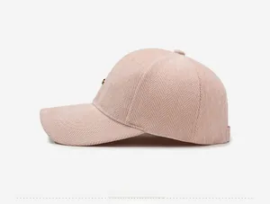 Detail of herringbone fabric texture and gold metal badge on dusty pink baseball cap