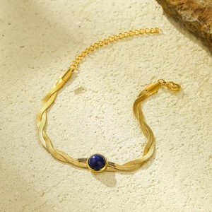 Detail of gold snake chains with center blue gemstone on textured stone surface