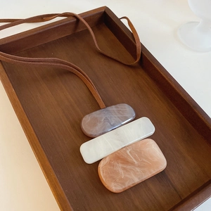 Close-up of irregular resin cube pendant with marble texture on brown suede cord