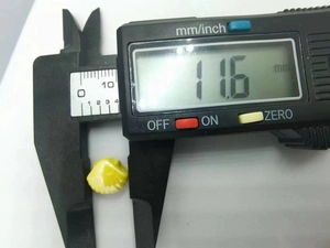 Macro shot of a yellow and white ceramic bead being measured with digital calipers at 11.6mm
