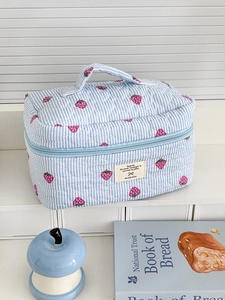 Detailed macro view of quilted strawberry pattern and logo patch on a blue striped toiletry bag