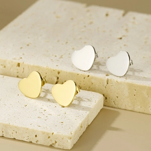 Macro view of gold and silver heart-shaped stainless steel earrings on beige travertine stone