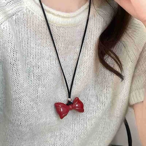 Close-up of a red bow pendant necklace with black cord on model wearing white sweater