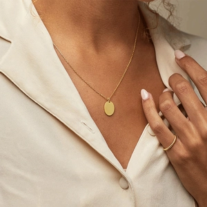 Polished gold stainless steel oval pendant necklace and twisted ring worn by model