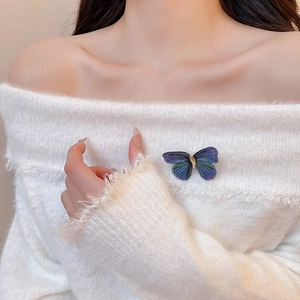 Detailed close-up of a blue embroidered butterfly brooch on a white sweater