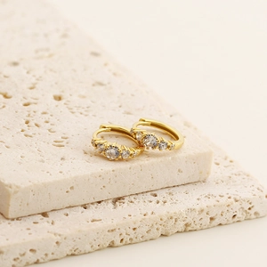 Macro detail of gold hoop earrings with sparkling zircon stones on natural stone slabs