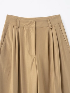 Detail of khaki high-waisted pleated trousers showing fabric texture and waistband design