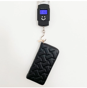 Vertical view of a black embossed leather wallet being weighed on a digital hanging scale