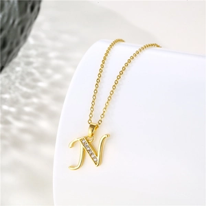 Detailed close-up of 18K gold letter N pendant with cubic zirconia on a white stand