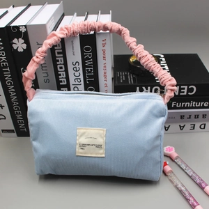 Close-up of light blue corduroy handbag with pink ruffled handle and minimalist label
