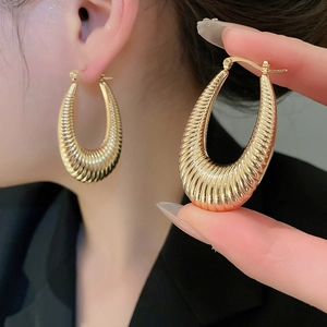 Detailed macro view of gold-toned oval hoop earrings featuring a rippled textured finish