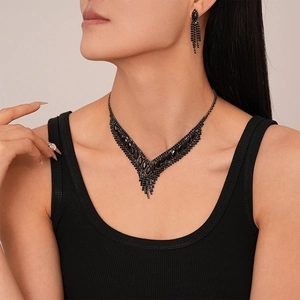 Close-up of a model wearing a black V-shaped rhinestone necklace and fringe tassel earrings