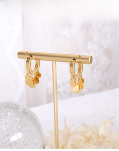 Close-up of golden hoop earrings with small disk charms on an elegant jewelry display stand