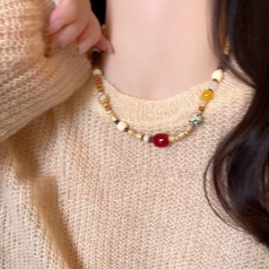 Detail einer ethnischen Perlenkette mit roten, gelben und gefleckten Steinperlen am Model