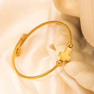 Golden titanium steel cable bracelet with a cross pendant on elegant beige silk fabric
