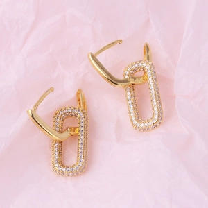 Elegant gold-tone oval hoop earrings with shimmering crystal pavé on soft pink background