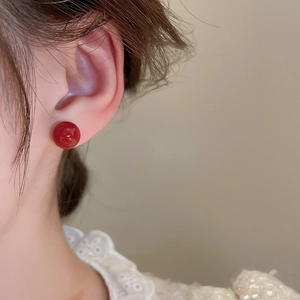 Close-up of minimalist red round bead stud earring worn by model showing glossy texture