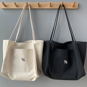 Minimalist canvas tote bags in cream and black hanging on a wooden hook stand