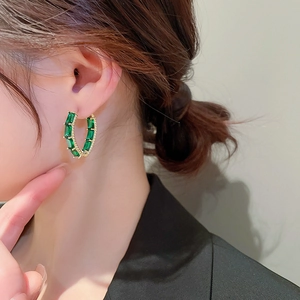 Close-up of gold geometric hoop earring with green zircon stone worn by a model