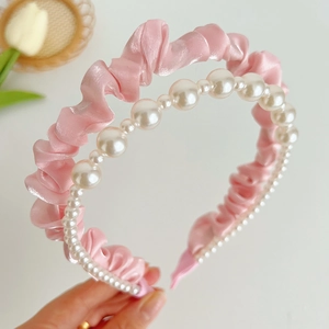 Pink satin headband with white pearl detailing shown in a detailed hand-held view