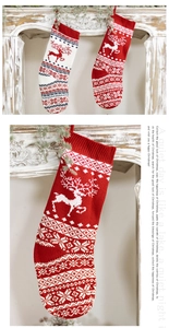 Detail of red and white knitted Christmas stocking with elk and snowflake by the fireplace