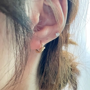 On-ear display of minimalist knotted gold hoop earring and sparkling stud on model