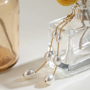 Elegant gold chain earrings with three white pearls shown in a professional studio setting